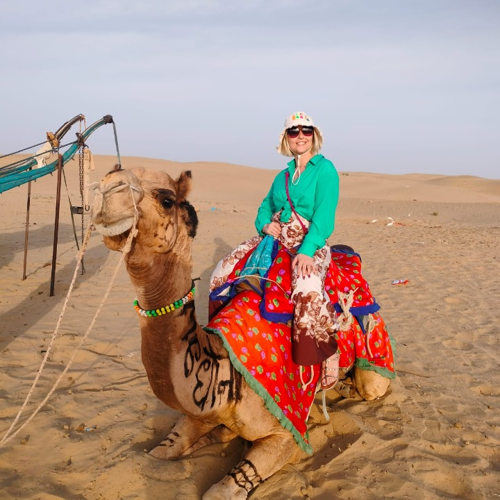 Turista straniero in sella a un cammello nel deserto del Thar al tramonto in Rajasthan, India