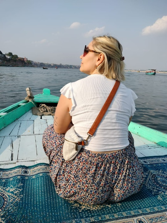 Ragazza italiana seduta su una tradizionale barca in legno durante un giro in barca all'alba sul fiume Gange a Varanasi, India.