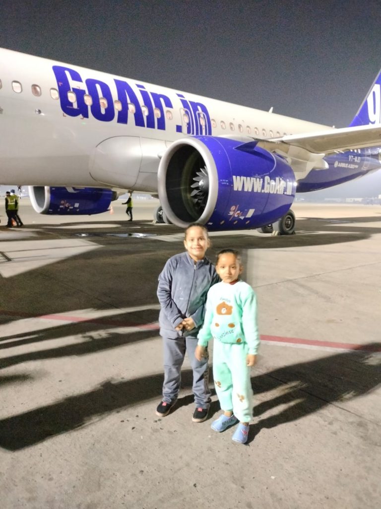 Duebambine sorridenti vicino a un aereo prima della partenza per un viaggio in India.